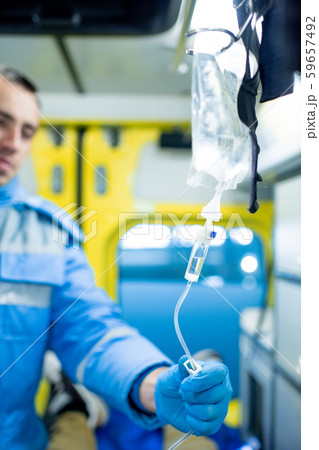 Gloved paramedic checking dropper while going to give first aid to sick person Gloved paramedic checking dropper while going to give first aid to sick person 59657492