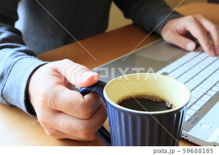マグカップのコーヒーを飲みながらノートパソコンで仕事をする 59688185