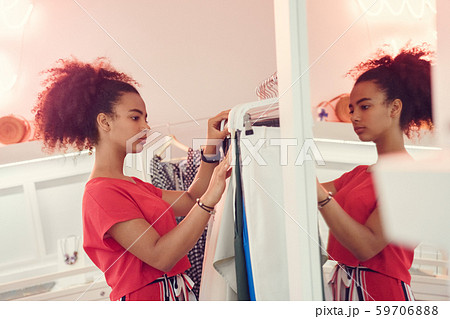 Choosing Clothes. African teenager girl standing choosing clothes from wardrobe looking at variety Choosing Clothes. African teenager girl standing choosing clothes from wardrobe looking at variety 59706888