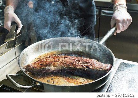 The chef works in the kitchen of the restaurant. Fresh meat roasted in a large frying pan 59711915