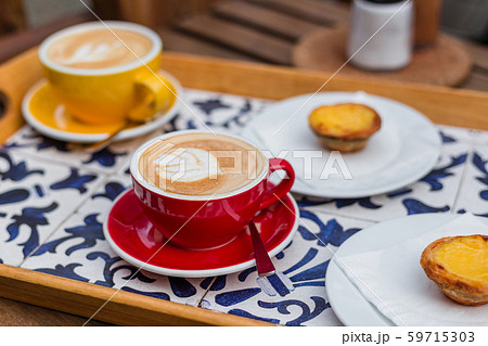 Two Cups of coffee latte in ceramic cups with traditional Portuguese dessert pastel de nata. Two Cups of coffee latte in ceramic cups with traditional Portuguese dessert pastel de nata. 59715303