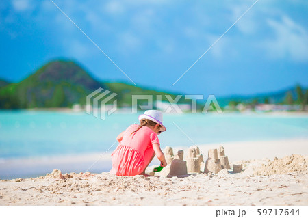 Little adorable girl at tropical beach making sand castle 59717644