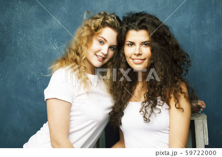 young pretty teenage girls friends with blond and brunette curly hair posing cheerful on blue 59722000