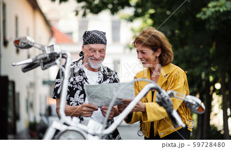 A cheerful senior couple travellers with motorbike in town, looking at map. 59728480