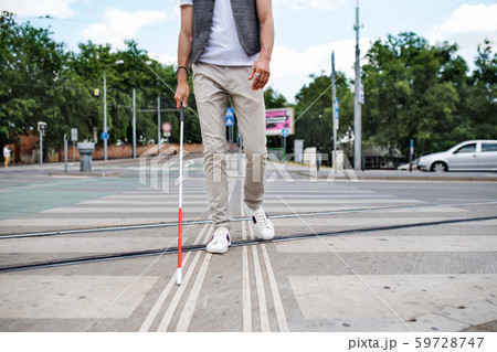 Midsection of young blind man with white cane walking across the street in city. 59728747