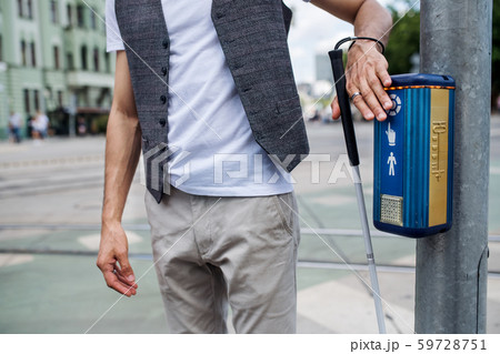 Midsection of young blind man with white cane walking across the street in city. 59728751