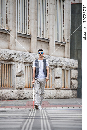 Young blind man with white cane walking across the street in city. Young blind man with white cane walking across the street in city. 59728756