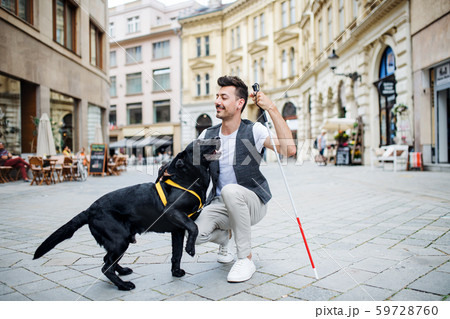 Young blind man with white cane and guide dog on pedestrain zone in city. 59728760
