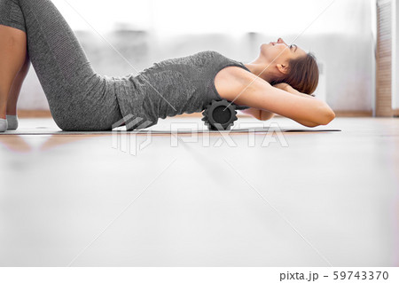 Girl doing yoga lying on massager on grey rug in gym 59743370