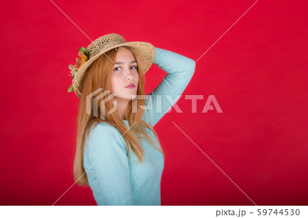 Portrait of a beautiful young red-haired woman in a straw hat, a girl posing on a red background in 59744530
