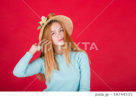 Portrait of a beautiful young red-haired woman in a straw hat, a girl posing on a red background in 59744535