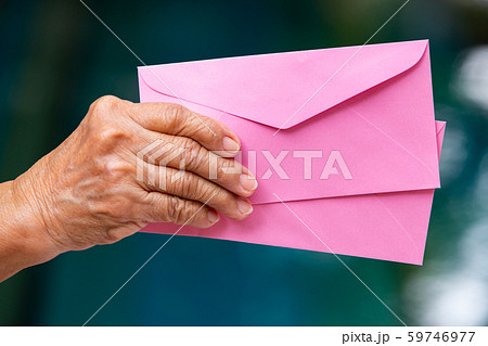 Senior woman's right hand holding 2 pink envelopes in bokeh blue swimming pool background, Close up shot Senior woman's right hand holding 2 pink envelopes in bokeh blue swimming pool background, Close up shot 59746977