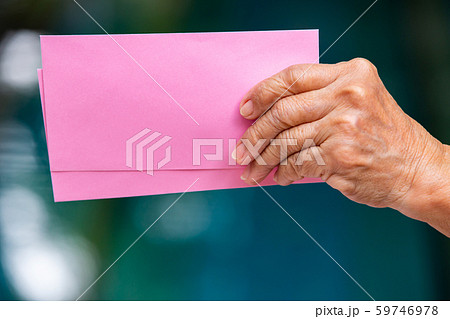 Senior woman's left hand holding 2 pink envelopes in bokeh blue swimming pool background, Close up shot 59746978