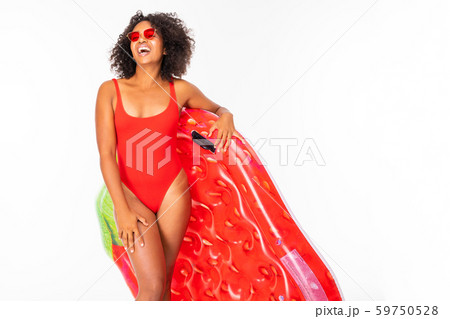 Pretty african female stands in swimsuit with rubber beach strawberry mattress and smiles isolated Pretty african female stands in swimsuit with rubber beach strawberry mattress and smiles isolated 59750528