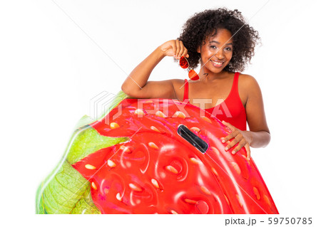 Pretty african female stands in swimsuit with rubber beach strawberry mattress and smiles isolated Pretty african female stands in swimsuit with rubber beach strawberry mattress and smiles isolated 59750785