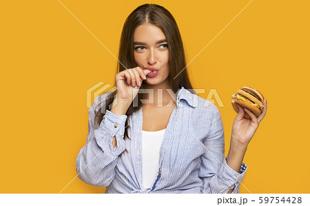 Hungry Girl Holding Burger Standing Over Yellow Background Hungry Girl Holding Burger Standing Over Yellow Background 59754428