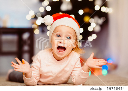 Happy emotional little girl in Santa hat lying on floor at home Happy emotional little girl in Santa hat lying on floor at home 59756454