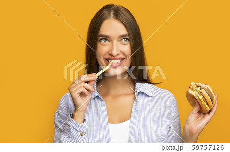 Happy Girl Eating Burger And French Fries Standing, Yellow Background 59757126