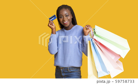 Happy african girl recommending credit card, holding shopping bags Happy african girl recommending credit card, holding shopping bags 59758733