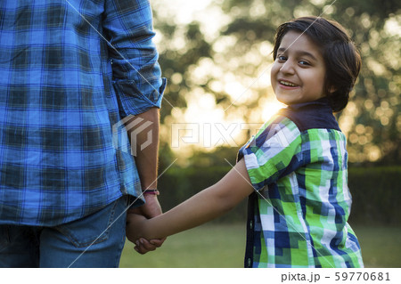 Rear view of a happy boy holding hand of his father standing in park. 59770681