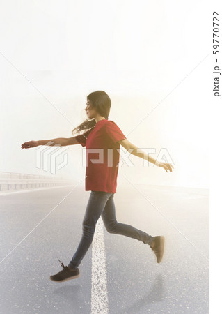 Young woman leaping joyfully in mid air across the road with sun in the background. Young woman leaping joyfully in mid air across the road with sun in the background. 59770722