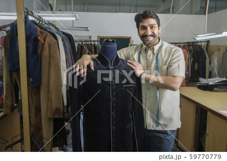 Tailor standing beside a mannequin wearing a semi-stitched coat in his workshop. Tailor standing beside a mannequin wearing a semi-stitched coat in his workshop. 59770779