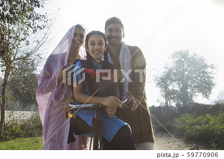 Low angle view of a happy rural family consisting of man, woman and a school going girl standing on pathway in a village. 59770906