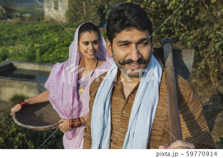 Close up of a village man going to agriculture field carrying a spade with his wife following him with an iron gold pan in hand. Close up of a village man going to agriculture field carrying a spade with his wife following him with an iron gold pan in hand. 59770914