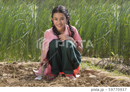 Happy little rural girl digging soil using a trowel sitting in agriculture field. Happy little rural girl digging soil using a trowel sitting in agriculture field. 59770937