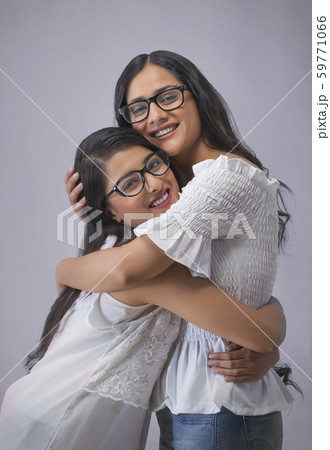 Two smiling young girls in spectacles standing opposite to each other and hugging 59771066