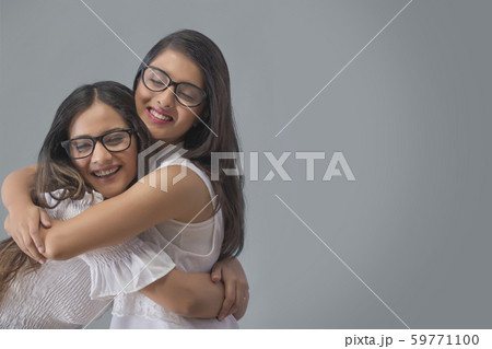 Two smiling young girls in spectacles hugging each other with eyes closed Two smiling young girls in spectacles hugging each other with eyes closed 59771100