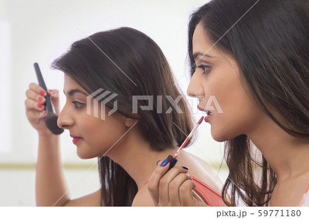 Side view of two teenage girls doing makeup applying lip paint and brush Side view of two teenage girls doing makeup applying lip paint and brush 59771180