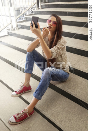 Woman applying lipstick sitting on steps 59771236