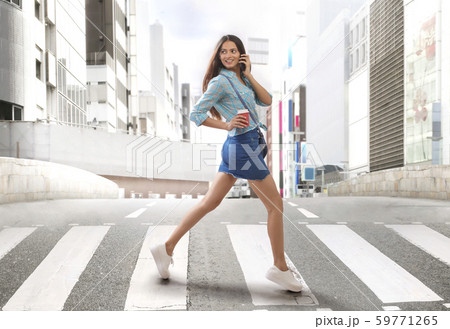 Woman crossing road on zebra crossing while talking on mobile phone 59771265