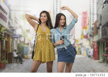 Two young women standing on street listening to music 59771352