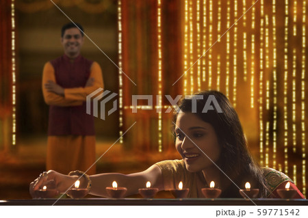 Woman decorating the house with diya on the occasion of diwali with husband standing in background 59771542