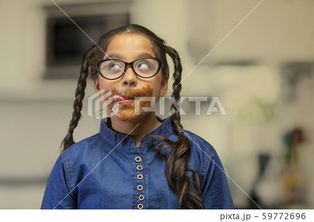 Girl wearing eyeglasses licking the chocolate around her mouth looking up 59772696