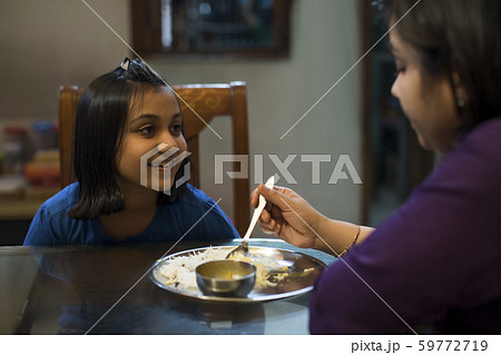 Young girl happily looks at her mother while she feeds her Young girl happily looks at her mother while she feeds her 59772719