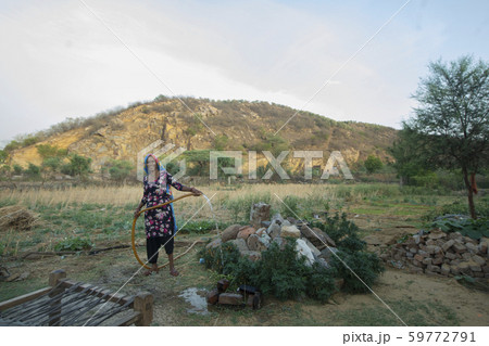 woman watering plants with a pipe, in the field 59772791