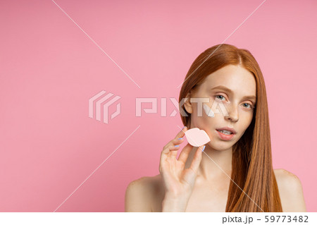 Portrait of young woman applying face cream and cleansing face with sponge Portrait of young woman applying face cream and cleansing face with sponge 59773482