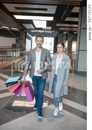 Couple smiling while leaving shopping center after successful shopping Couple smiling while leaving shopping center after successful shopping 59774120