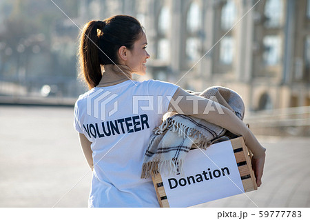 Dark-haired volunteer caring box with old clothing and plaid Dark-haired volunteer caring box with old clothing and plaid 59777783