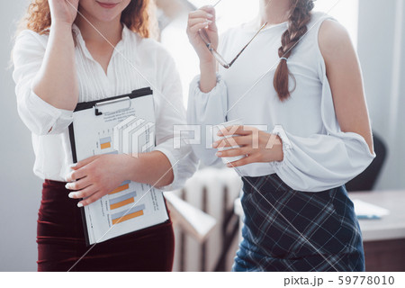 Beautiful women in the office in business clothes, one of them holds documents in his hands. Beautiful women in the office in business clothes, one of them holds documents in his hands. 59778010