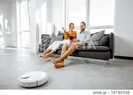 Young couple relaxing while automatic vacuum cleaner working at home Young couple relaxing while automatic vacuum cleaner working at home 59780506