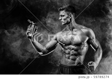 Muscular man with protein drink in shaker over dark smoke background Muscular man with protein drink in shaker over dark smoke background 59789274