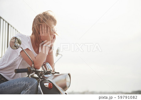 Portrait of a beautiful girl hipster sitting on a black retro scooter, smiling posing and enjoy the 59791082