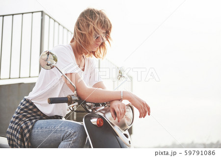 Portrait of a beautiful girl hipster sitting on a black retro scooter, smiling posing and enjoy the 59791086