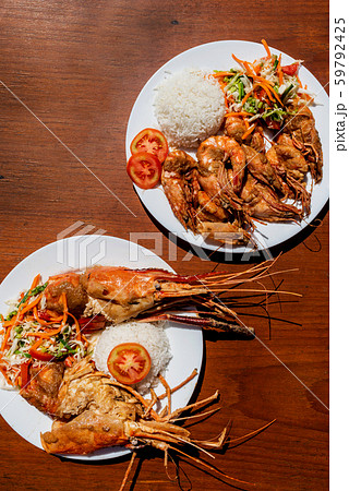 Plates with king prawns and fried ocean fish with side dish and salad on a wooden table. Plates with king prawns and fried ocean fish with side dish and salad on a wooden table. 59792425