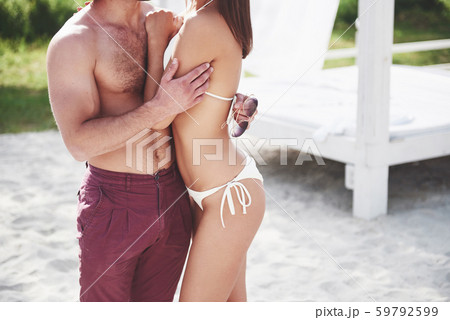 A beautiful couple relaxing on the sandy beach, wearing bathing clothes. Romantic atmosphere A beautiful couple relaxing on the sandy beach, wearing bathing clothes. Romantic atmosphere 59792599