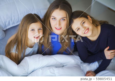 Happy family playing at home. Mother and toddler daughters relaxing and having fun in bed in cozy 59805451